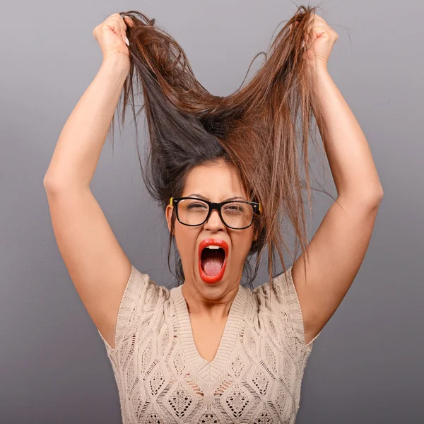 Portrait of a histerical woman pulling hair out against gray bac