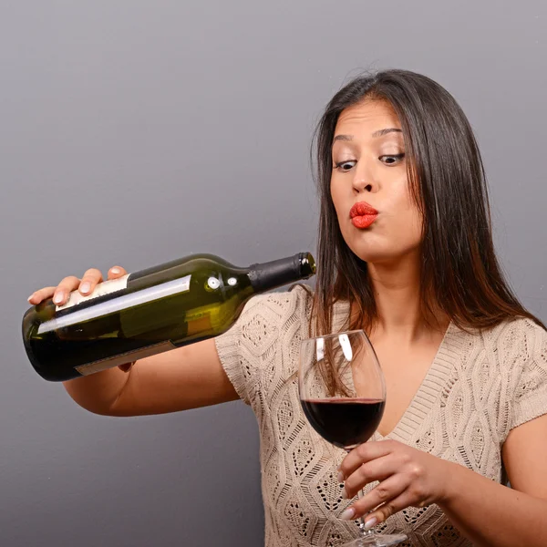 Portrait of woman holding wine bottle and glass against gray bac