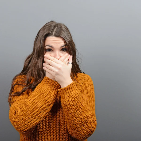 Woman covering her mouth with hands against  gray background