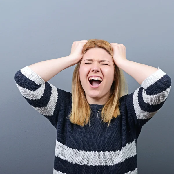 Portrait of a histerical woman pulling hair out against gray bac