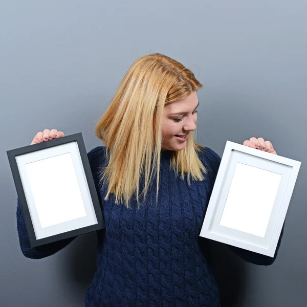 Portrait of smiling woman holding blank photo frames against gra