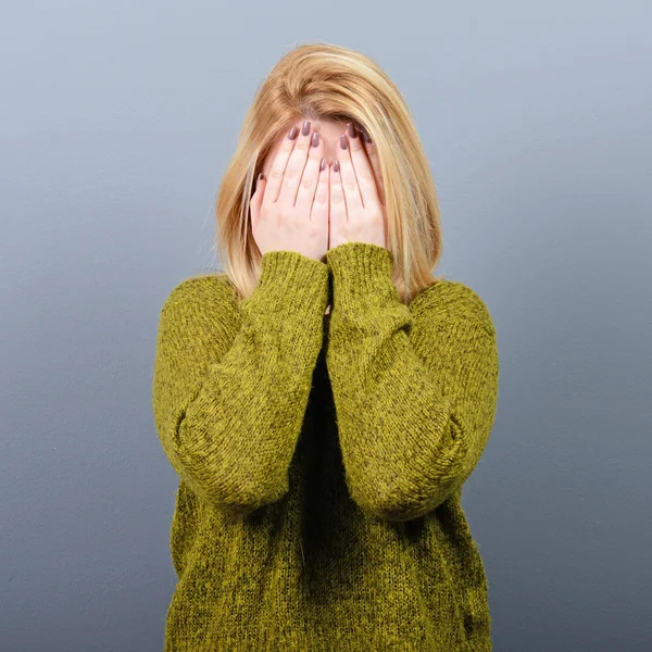 Portrait of woman hiding her face with both hands against gray b