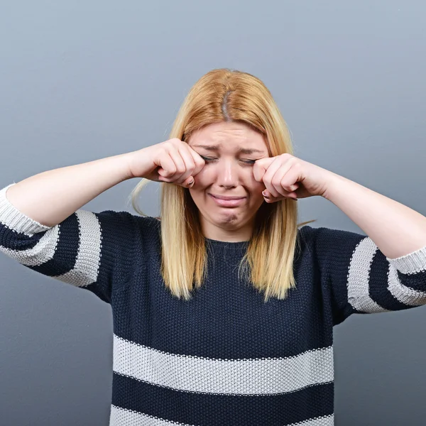 Woman crying and wiping tears against gray background