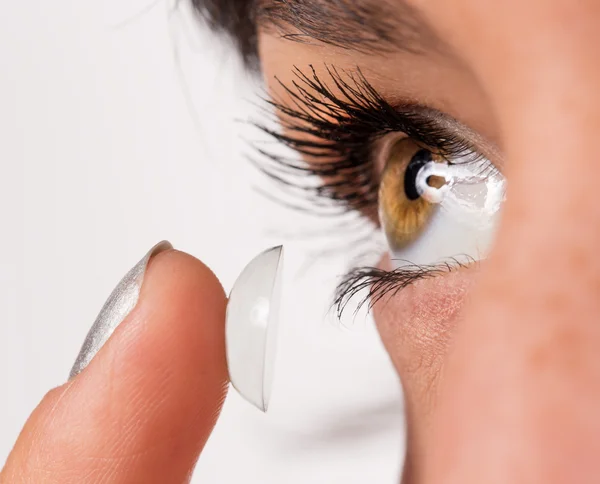 Young woman putting contact lens in her eye.