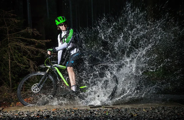 Mountain biker speeding through forest stream.