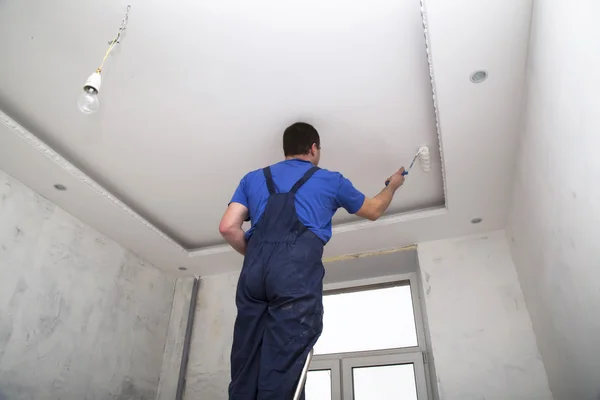 Man worker paints the ceilin inside of the room interior