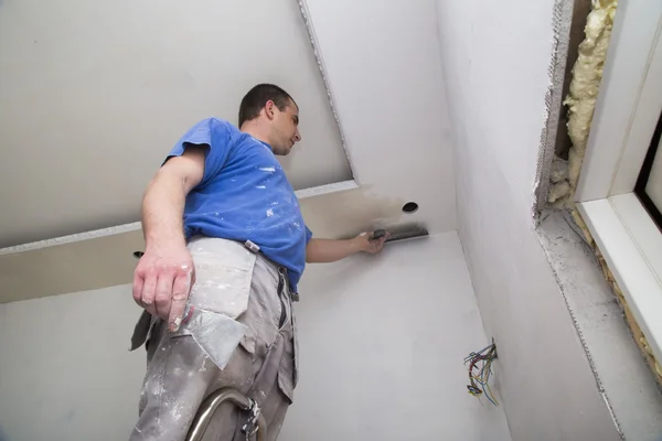 Plasterer with putty knife working on apartment wall