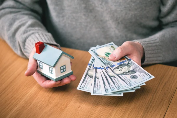 House and money. buy real estate, home mortgage. hands holding new hundred-dollar bills and toy house. Real estate agent