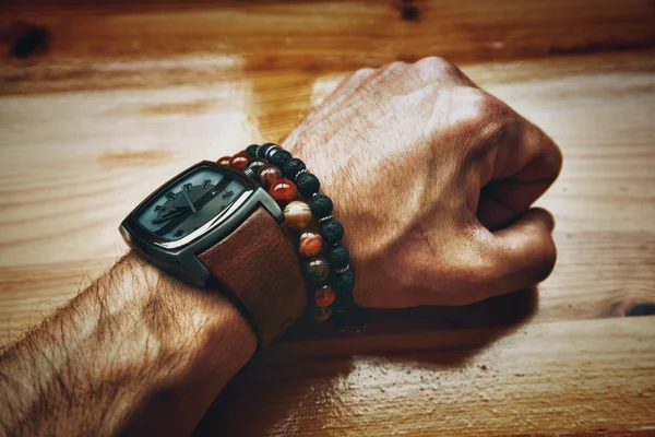 Man\'s hand with clock closeup. compressed brutal male fist. Bracelets - jewelry agate stone and lava stone on the hand. Fashionable men\'s accessories and jewelry