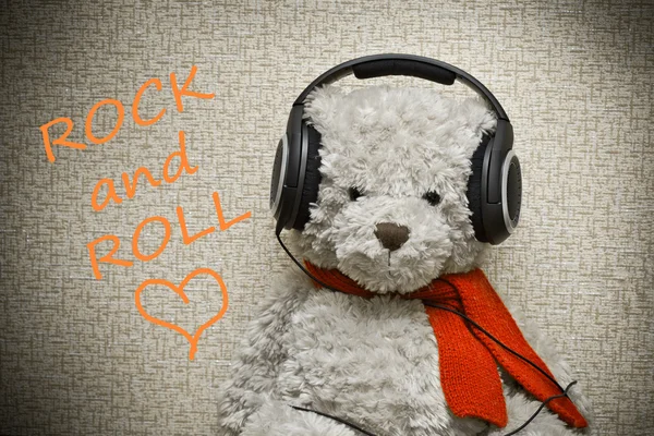 Teddy Bear with orange scarf listening to music on headphones. Lover of rock and roll