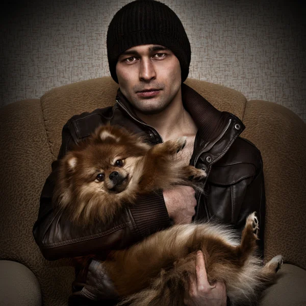 Brutal man in a hat and leather jacket with a dog in her arms