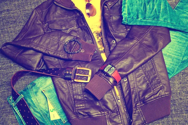 Clothing items and accessories: blue jeans with a leather belt, leather jacket, T-shirt, watches, sunglasses and a bracelet on a hand