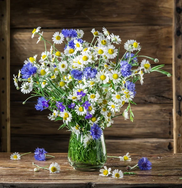 Bouquet of chamomiles and cornflowers in the vase on the wooden