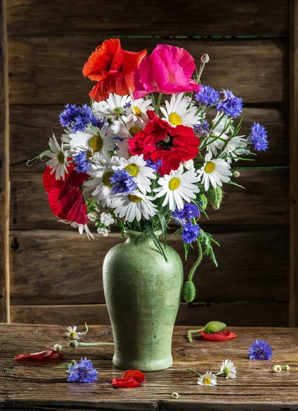Bouquet of field flowers in the vase on the wooden table.