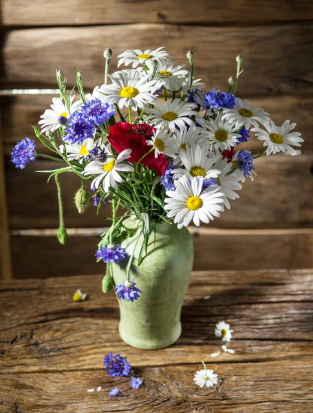 Bouquet of field flowers in the vase on the wooden table.