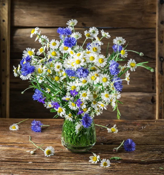 Bouquet of chamomiles and cornflowers in the vase on the wooden