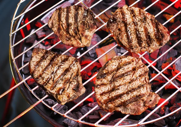 Pieces of sirloin are grilling on the barbecue.