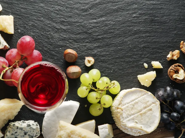 Different types of cheeses with wine glass and fruits.