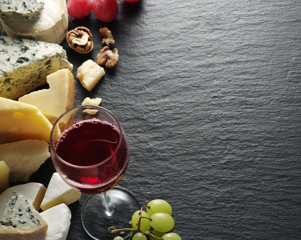 Different types of cheeses with wine glass and fruits.