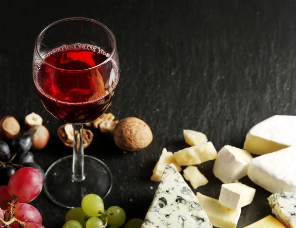 Different types of cheeses with wine glass and fruits.