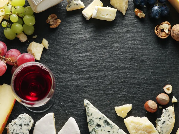 Different types of cheeses with wine glass and fruits.