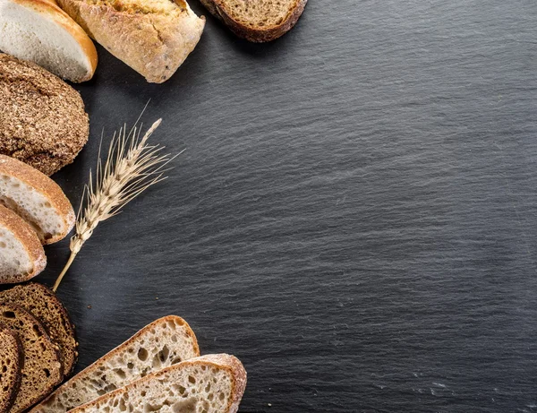 Bread slices, a wheat and a knife on the black stone desk.