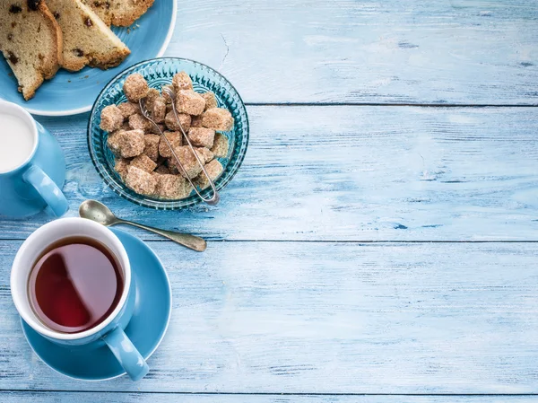 Cup of tea, milk jug and cane sugar cubes.