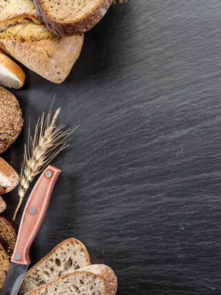 Bread slices, a wheat and a knife on the black stone desk.