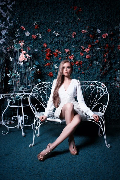 Fashion and beautiful young woman in a green wall of flowers and leaves