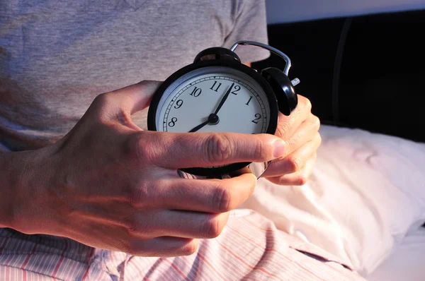 Young man in bed setting the alarm clock