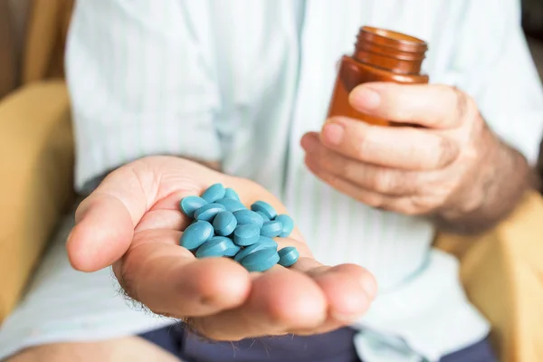 Old man with a pile of blue pills in his hand