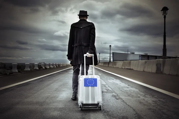 Young man with a rolling suitcase with an European flag