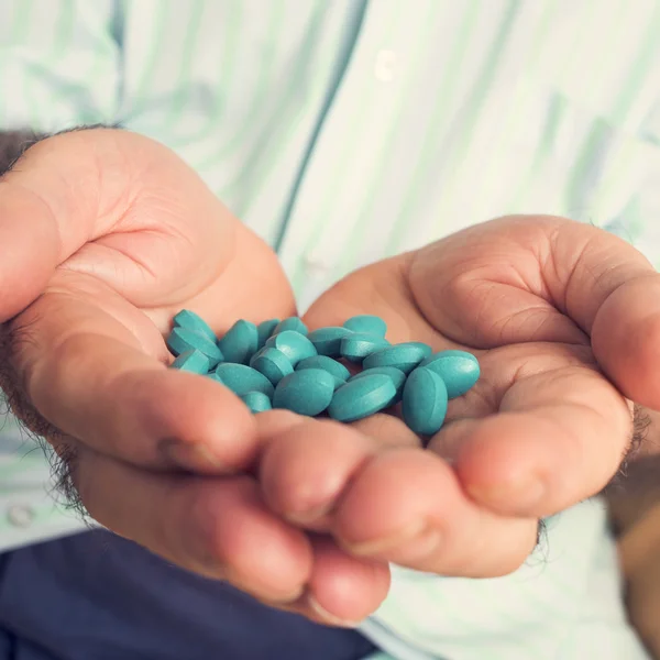 Old man with a pile of blue pills in his hand