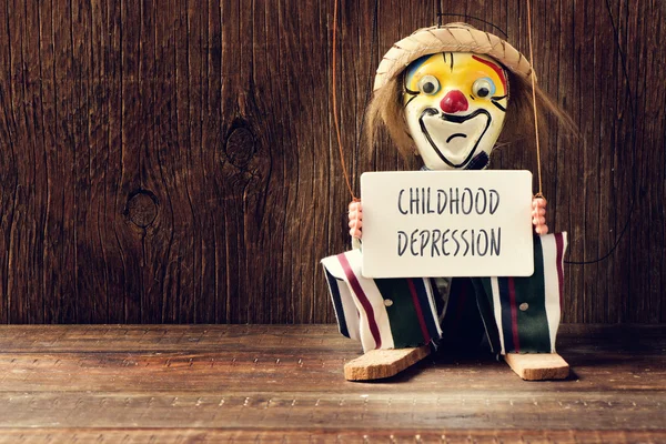 Old marionette with a signboard with the text childhood depression