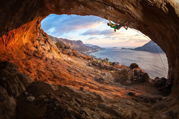 Male rock climber climbing along a roof in a cave at sunset