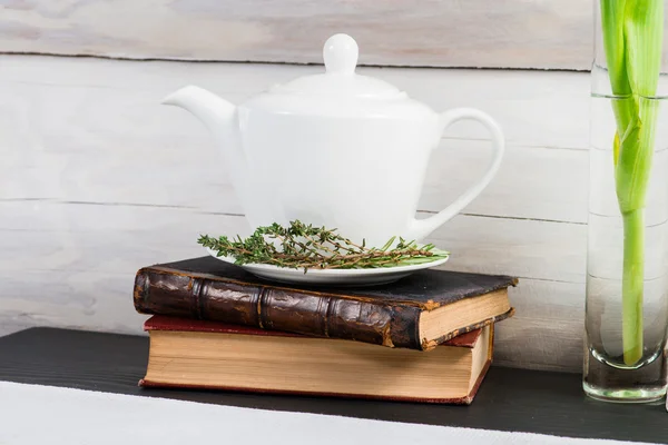 White teapot with green leaves herbal tea and old books