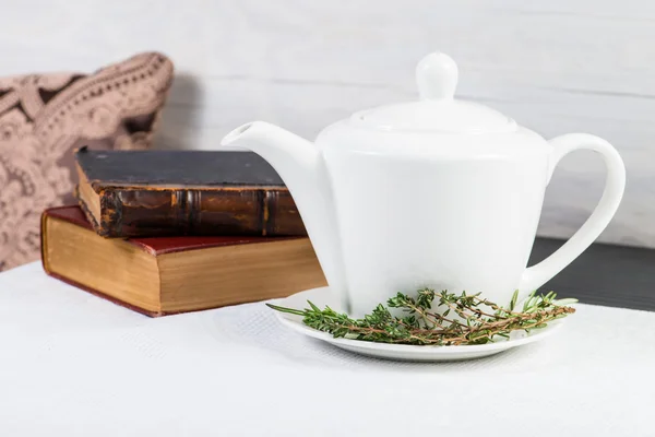 White teapot with green leaves herbal tea and old books
