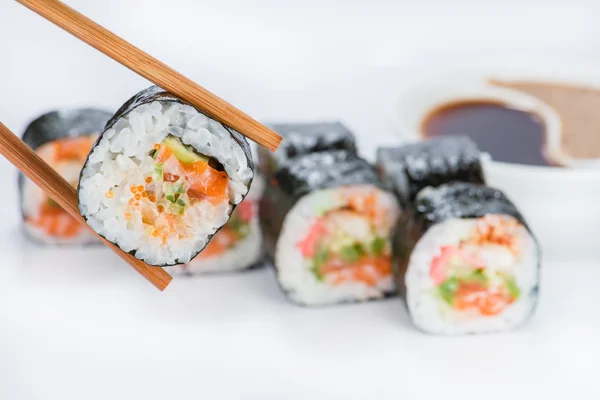 Close up of chopsticks taking portion of sushi roll on the table