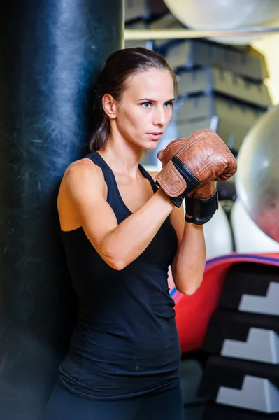 Beautiful sporty woman boxing with black punching bag at gym.