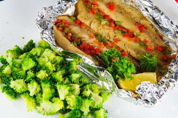 Plate of baked fish with vegetables in foil .Close up.