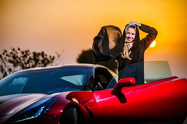 Arabic way dressed yang woman posing in red car in desert.