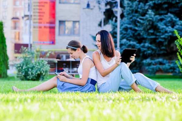 Mother is reading from tablet with her daughter, outdoor shoot
