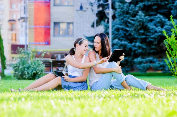 Mother is reading from tablet with her daughter, outdoor shoot