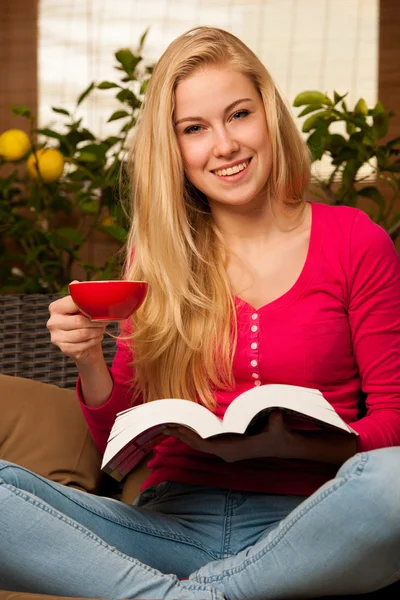 Woman comfortable sitting on sofa, reading book and drinking tea