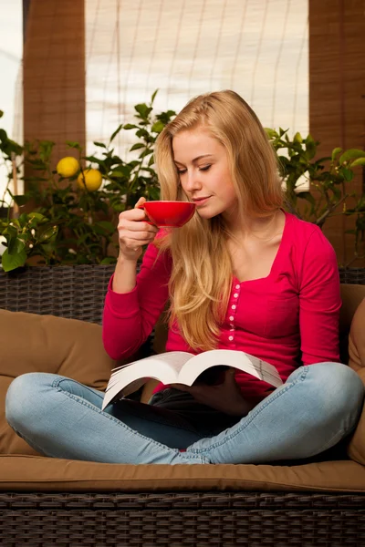 Woman comfortable sitting on sofa, reading book and drinking tea