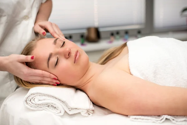 Young woman lying on massage table receiving face massage. Beaut