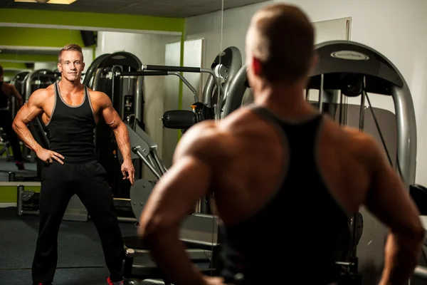 Handsome man looking in mirror after body building workout in fi