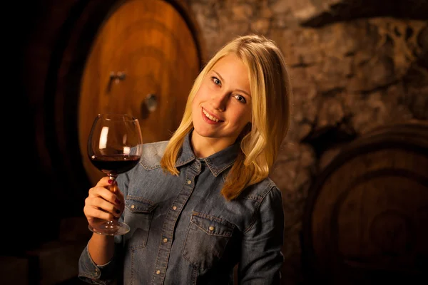 Beautiful young blond woman tasting red wine in a wine cellar