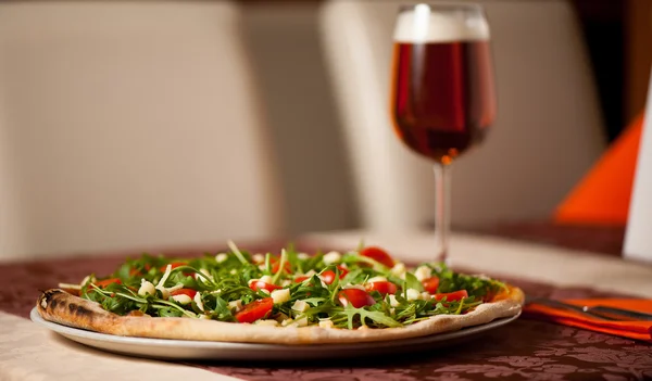 Pizza with rucola, cherry tomatoes and a glass of beer on a tebl