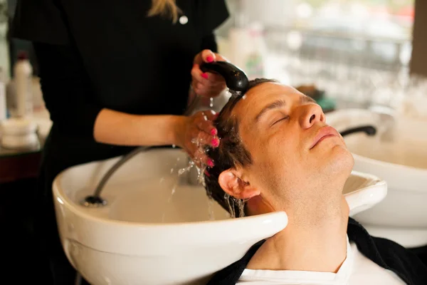 Female hairdresser washing hair of smiling man client at beauty